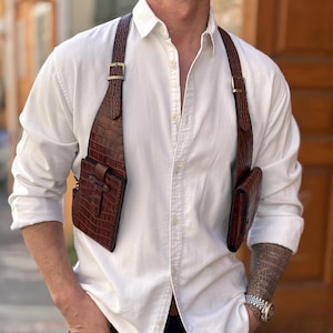 May include: A brown leather crossbody bag with a crocodile pattern. The bag has two separate compartments and is worn over the shoulder.
