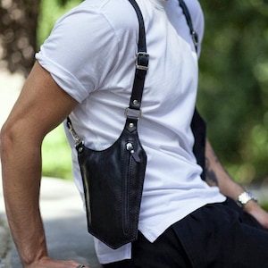 Peut inclure: Holster d'épaule en cuir noir avec une poche verticale zippée et des sangles réglables. L'étui est conçu pour être porté en travers de la poitrine et sur l'épaule. Les sangles ont des boucles et des accessoires métalliques.