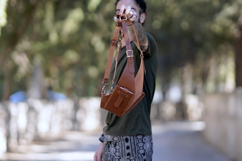 May include: A brown leather crossbody bag with adjustable straps and a flap closure. The bag has a small pocket on the front and a larger pocket on the back.