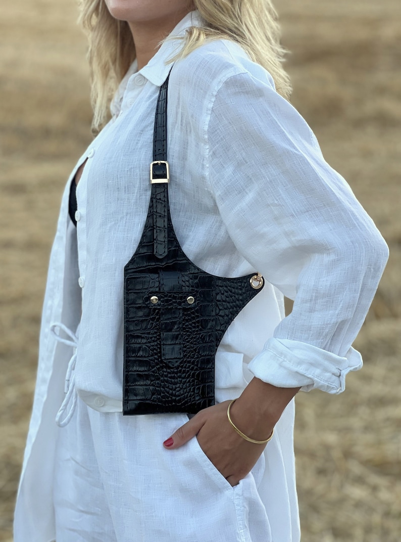May include: A black leather crossbody bag with a crocodile-embossed design. The bag has a gold buckle and a gold chain strap.
