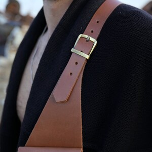 May include: A brown leather strap with a brass buckle, worn over a black sweater.