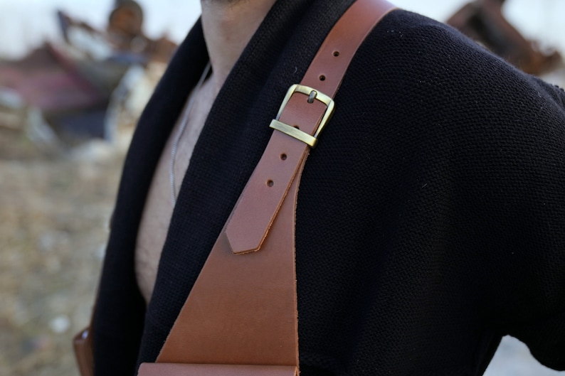May include: A brown leather strap with a brass buckle, worn over a black sweater.
