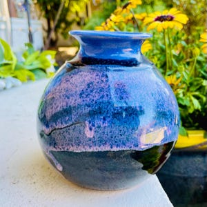 May include: A small, round ceramic vase with a blue and purple glaze. The vase has a wide mouth and a narrow neck.