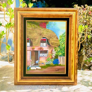 May include: Framed painting of a quaint cottage with a thatched roof, surrounded by colorful flowers and greenery. The artwork features a gold-colored frame and a black matting, creating a classic and charming aesthetic. The painting is signed in the lower right corner.