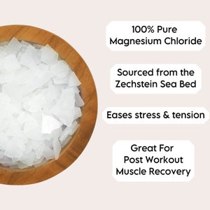 Op de afbeelding: Een houten kom gevuld met witte magnesiumchloride vlokken. De tekst "100% Pure Magnesium Chloride", "Sourced from the Zechstein Sea Bed", "Eases stress & tension" en "Great For Post Workout Muscle Recovery" wordt rond de kom weergegeven.
