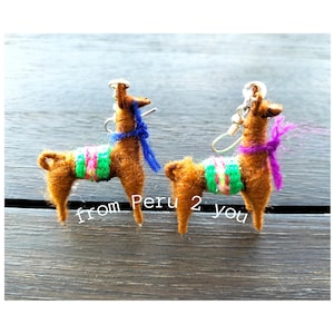 Könnte beinhalten: Ein Paar braune Lama-Ohrringe mit bunten gewebten Bändern und blauen und violetten Quasten. Die Ohrringe sind handgefertigt und haben silberne Ohrhaken.