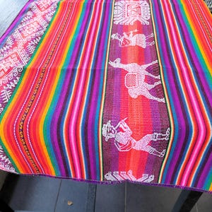 May include: A colorful woven tapestry with a geometric pattern and white figures of people and animals. The tapestry is made of a variety of colors, including red, orange, yellow, green, blue, purple, and white.