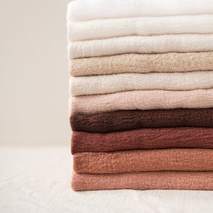 May include: A stack of folded fabric cloths in various shades of brown, beige, and white. The cloths are arranged from lightest to darkest, with the white cloths on top and the darkest brown cloths on the bottom.