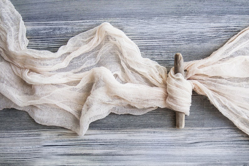 May include: A piece of white gauze fabric tied with a piece of driftwood on a gray wooden background.