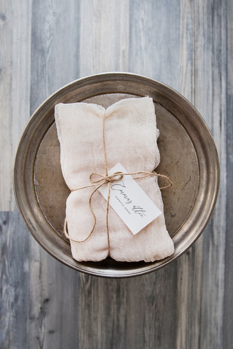 May include: A white cloth bundle tied with twine and a small white tag that reads "Envoy Attic Fantastic Goods". The bundle is sitting on a silver tray.