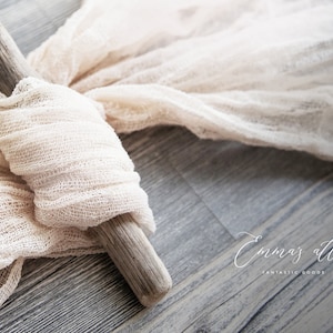 May include: A piece of white gauze fabric draped over a piece of driftwood. The fabric is textured and has a natural, rustic look. The driftwood is light brown and has a rough surface. The fabric and driftwood are on a gray wooden surface. The text "Emma's Attic Fantastic Goods" is visible in the lower right corner of the image.