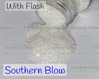 May include: A clear glass jar filled with iridescent white glitter. The jar is tipped over, spilling the glitter onto a white surface. The text "With Flash" and "Southern Blow" are visible in the image.