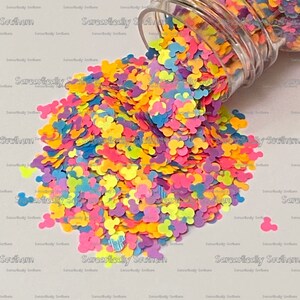 May include: A clear glass jar filled with colorful Mickey Mouse shaped confetti. The confetti is in shades of pink, blue, yellow, green, and orange.