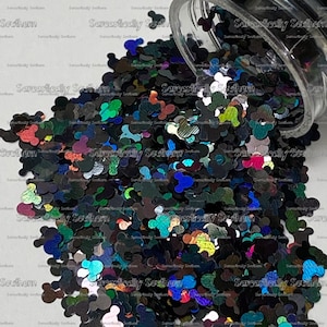 May include: A clear jar filled with iridescent black and multi-colored glitter shaped like Mickey Mouse heads. The glitter is spilling out of the jar onto a white surface.