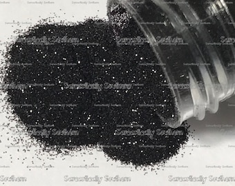 May include: A clear glass jar filled with black glitter. The glitter is spilling out of the jar onto a white surface.