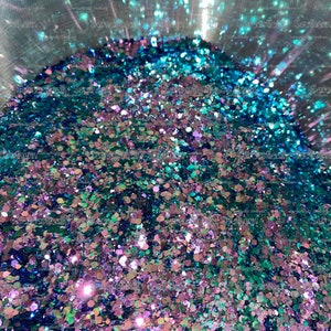 May include: A close-up of a container filled with iridescent glitter. The glitter is a mix of teal, blue, green, and purple colors.