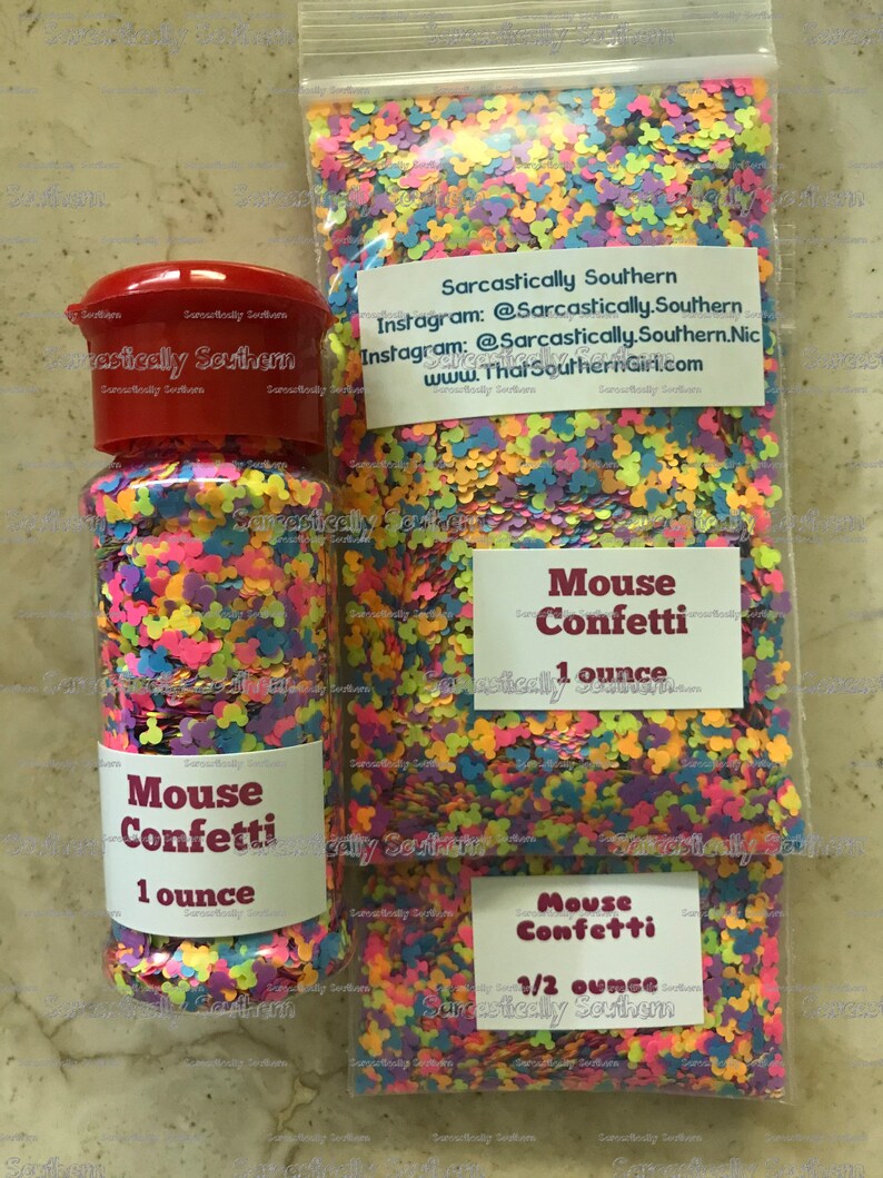 May include: Two containers of colorful confetti shaped like Mickey Mouse heads. The smaller container is labeled "Mouse Confetti 1/2 ounce" and the larger container is labeled "Mouse Confetti 1 ounce".