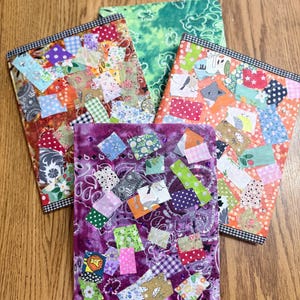 May include: A collection of four handmade journals with fabric patchwork covers. The journals feature a variety of colorful patterns, including floral, polka dots, and paisley. Each journal is rectangular and has a black and white checkered border.