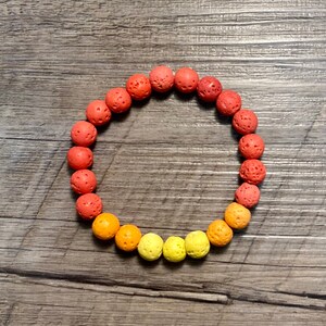 Peut inclure: Un bracelet en perles de roche volcanique rouge, orange et jaune. Les perles sont rondes et ont une surface texturée.