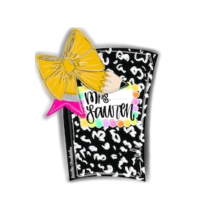 May include: A black and white leopard print pocket with a yellow bow and a pink pencil with the text "Mrs. Lauren" on it.
