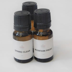 May include: Three small amber glass bottles with black caps. Two bottles have white labels with the text "Spring Clean" and "Mountain Fresh". The bottles are likely essential oils or aromatherapy products.