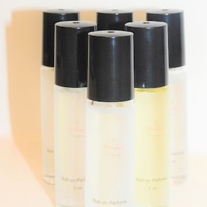 May include: Six clear glass roll-on perfume bottles with black caps. Each bottle contains a clear liquid and has a label that reads "Roll on Perfume 3 ml".