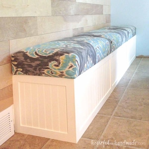 May include: White bench with a blue and gray patterned cushion. The bench has a white wood panel front and is built into a wall.