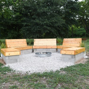 May include: Three wooden benches with concrete bases surround a fire pit in a gravel area. The benches are made of natural wood and have a simple design. The fire pit is made of metal and is surrounded by gravel.