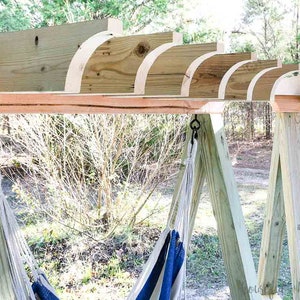 May include: A wooden hammock stand with two hammocks hanging from it. The stand is made of natural wood and has a rustic look. The hammocks are white with blue stripes.