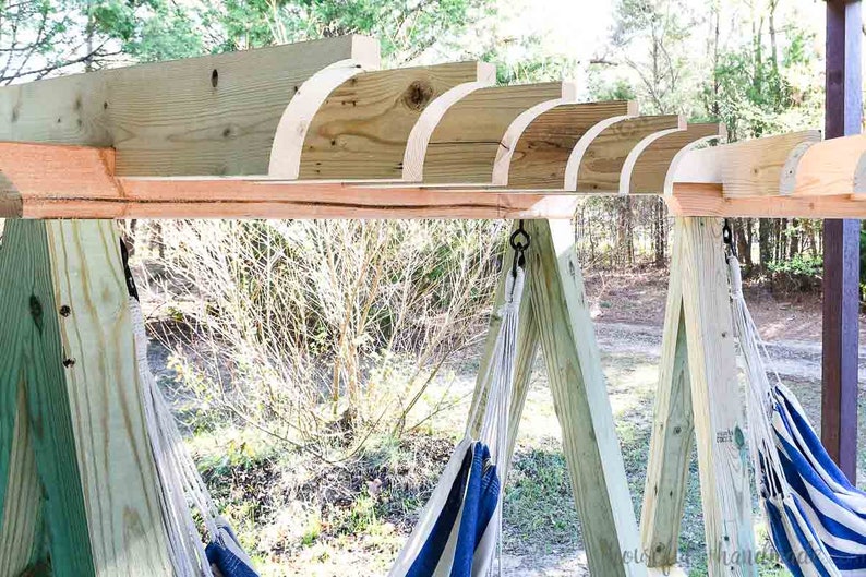 May include: A wooden hammock stand with two hammocks hanging from it. The stand is made of natural wood and has a rustic look. The hammocks are white with blue stripes.