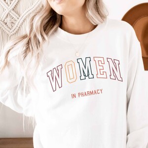 May include: White long-sleeve sweatshirt with the text "WOMEN IN PHARMACY" in colorful block letters.