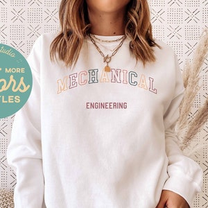 May include: White sweatshirt with the text "MECHANICAL ENGINEERING" in rainbow colors. The text is in an arch shape. The sweatshirt is on a person wearing black pants.