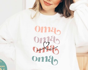 May include: White sweatshirt with the word "oma" repeated four times in different colors and fonts. The word "oma" is stacked vertically with a heart symbol between the second and third "oma".