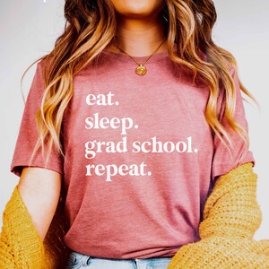 May include: A pink t-shirt with the text "eat. sleep. grad school. repeat." in white lettering.