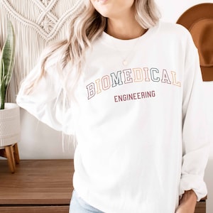 May include: White long-sleeved sweatshirt with the text "BIOMEDICAL ENGINEERING" in a rainbow arch design.
