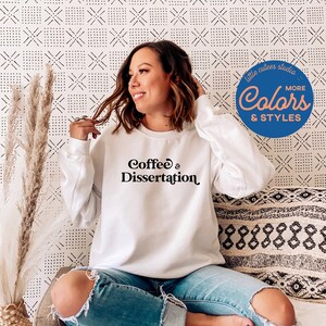 May include: White sweatshirt with the text "Coffee & Dissertation" in black. The model is wearing the sweatshirt and sitting on a couch.