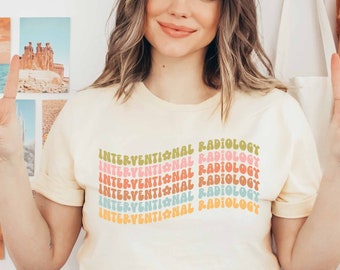 Puede incluir: Una camiseta amarilla clara con el texto "INTERVENTIONAL RADIOLOGY" repetido en un arcoíris de colores. El texto está en un estilo de fuente retro.