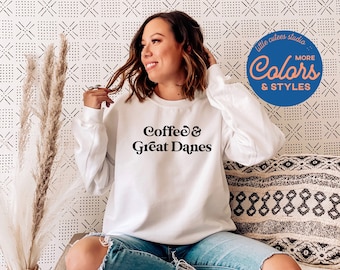 Könnte beinhalten: Ein weißer Pullover mit dem Aufdruck "Coffee & Great Danes" in Schwarz. Das Model trägt den Pullover und sitzt auf einem Sofa.