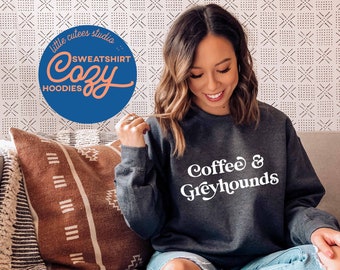 May include: A dark gray sweatshirt with the text "Coffee & Greyhounds" in white. The sweatshirt is being worn by a person sitting on a couch.
