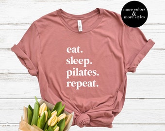 May include: A dusty rose t-shirt with the text "eat. sleep. pilates. repeat." printed in white.