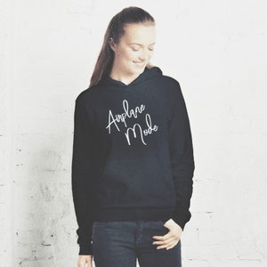 Op de afbeelding: Een zwarte hoodie met de tekst "Airplane Mode" in witte cursieve letters.