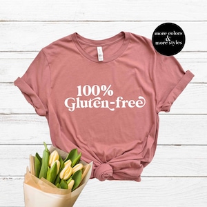 May include: A dusty rose t-shirt with the text "100% Gluten-free" in white. The shirt is made of a soft, comfortable material.