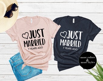 Puede incluir: Dos camisetas, una rosa pálido y otra azul marino, con el texto blanco "JUST MARRIED 7 YEARS AGO" y un corazón. También se ven unas gafas de sol y unos vaqueros azules.
