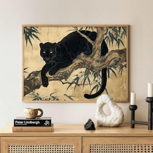 May include: A framed art print featuring a black panther resting on a tree branch. The artwork has a gold background with green foliage accents. The print is displayed on a wooden cabinet with decorative items.