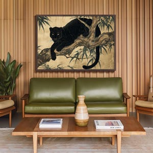 May include: A framed artwork featuring a black panther resting on a tree branch, set against a gold background with bamboo leaves. The artwork is displayed above a green leather sofa and wooden coffee table.