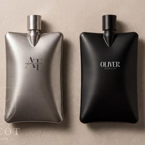 May include: Two rectangular, slightly concave metal flasks with rounded corners and narrow necks. The left flask is metallic silver with the text AT ANDREW THONG, and the right flask is matte black with the text OLIVER GARCIA. A logo with the text ASCOT ATELIER is visible.