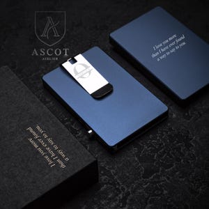 May include: A set of three metal money clips and cases. The blue clip has a silver money clip with the letter "O" on it. The cases are blue and black, with the text "I love you more than I have ever found a way to say to you."