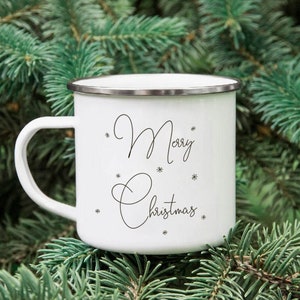 Puede incluir: Taza de esmalte blanco con una inscripci&oacute;n negra que dice "Feliz Navidad" rodeada de peque&ntilde;os dise&ntilde;os de copos de nieve.