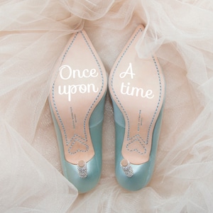 May include: A pair of light blue high-heeled shoes with the words "Once upon a time" written on the soles.