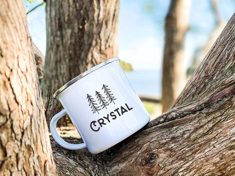 May include: White enamel camping mug with a black silhouette of three pine trees and the word "CRYSTAL" printed on the side.